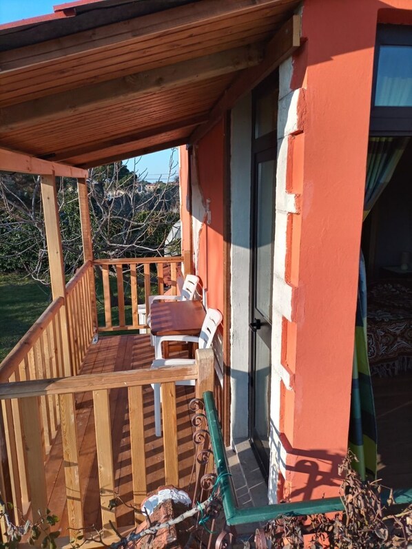 Eine Holzterrasse mit Tisch und Stühlen, einem überdachten Bereich und einem Gebäude mit roter Fassade.
