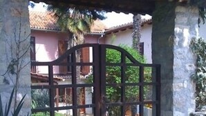 A gated entrance with a metal gate, a stone pillar, and a building with a tiled roof in the background. - Apartment Nives (Umag)