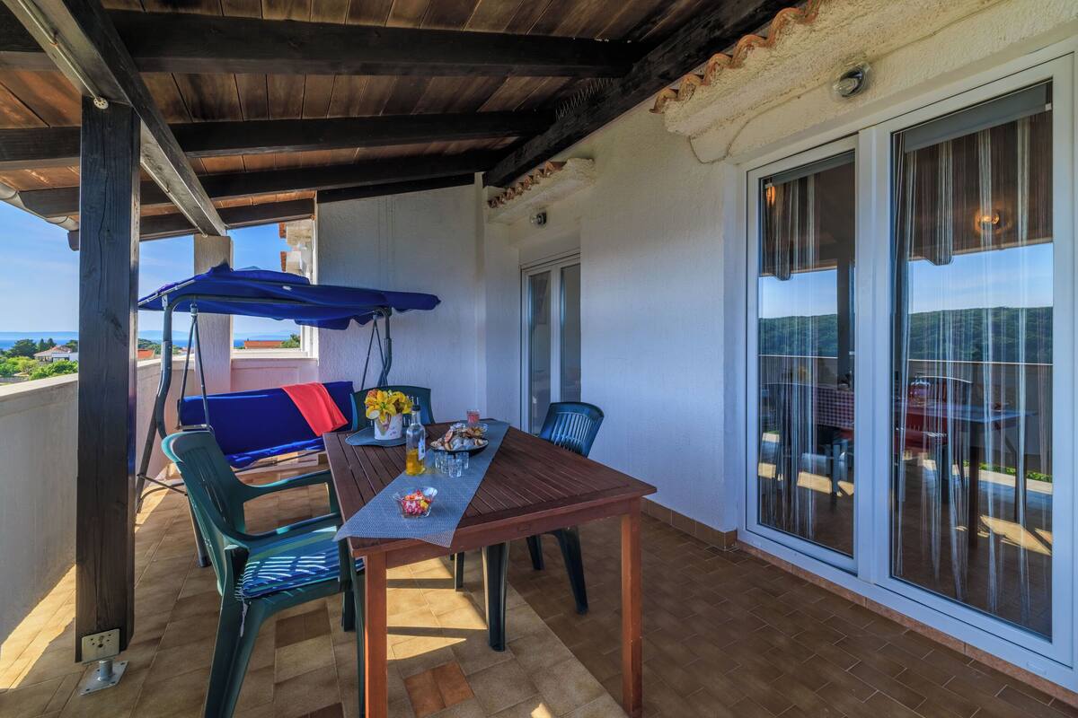 Une terrasse extérieure avec une table et des chaises en bois, un parasol bleu et une vue sur la mer.