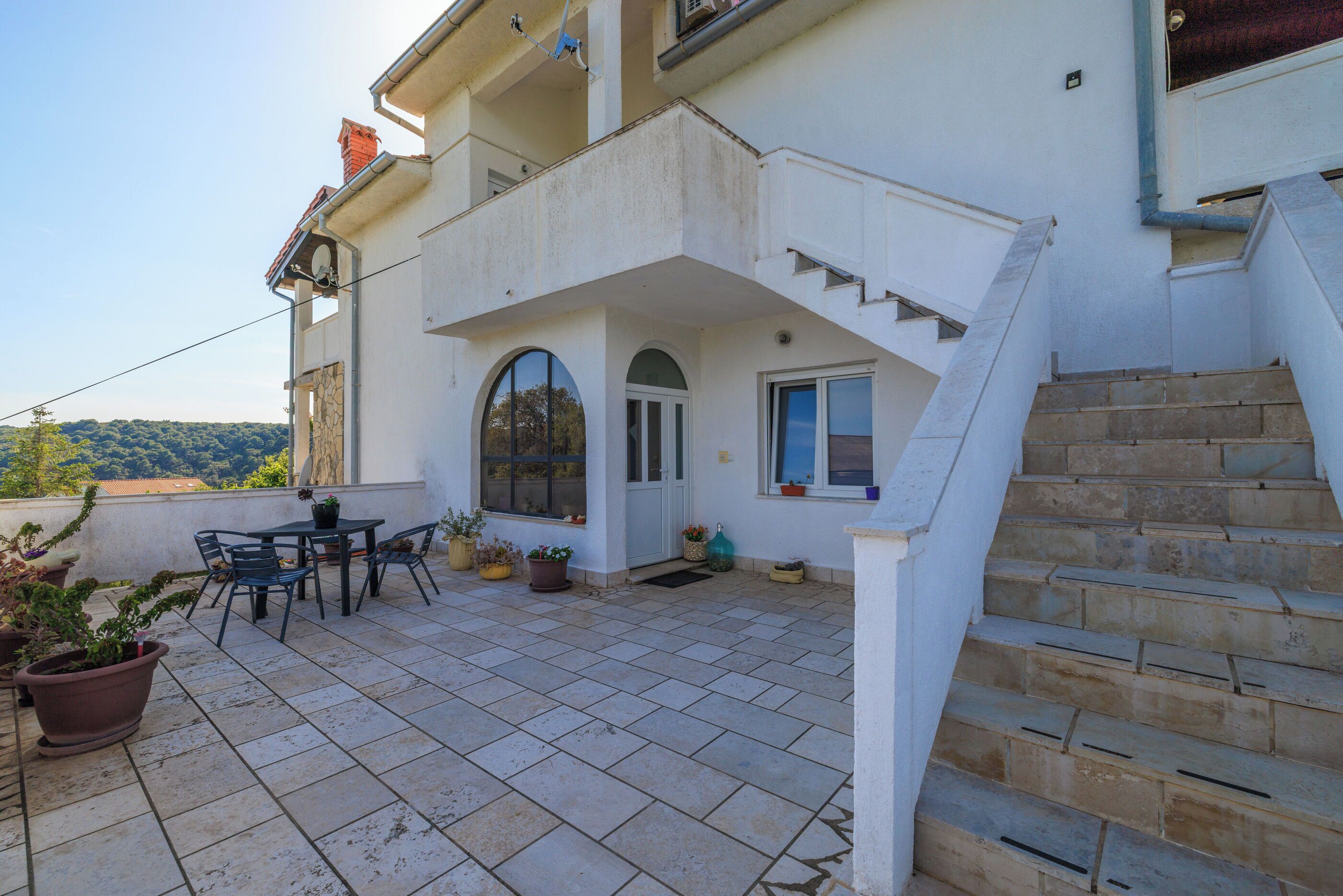 A residential building with a tiled patio, outdoor seating, and a staircase leading to an upper floor.