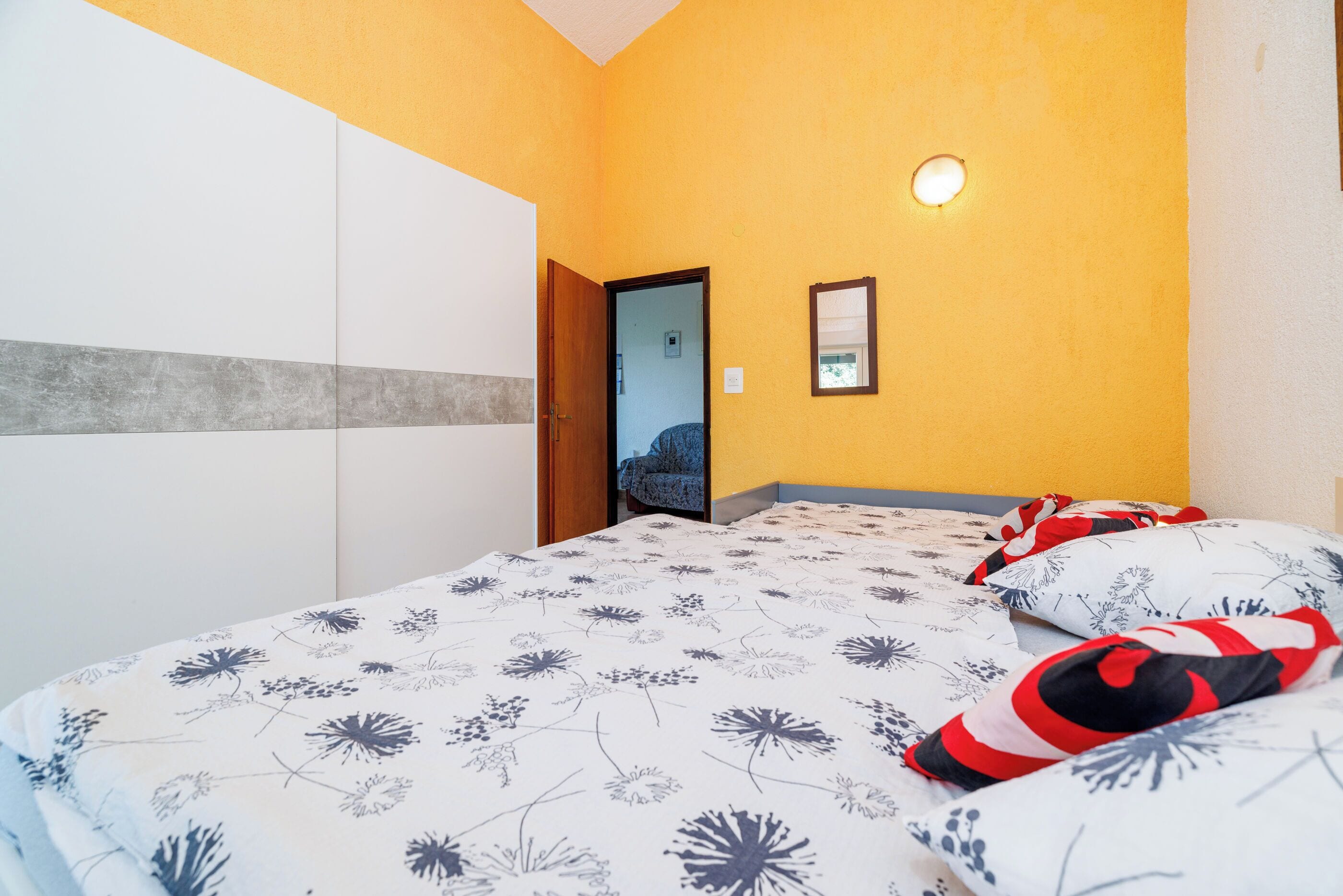 Ein Schlafzimmer mit einem Bett, einem Kleiderschrank, einem Spiegel und einer Tür zu einem anderen Raum.