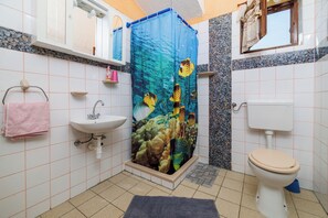 A bathroom with a shower curtain depicting tropical fish, a sink, a toilet, and a small window. - Apartments Davorka (Rab)
