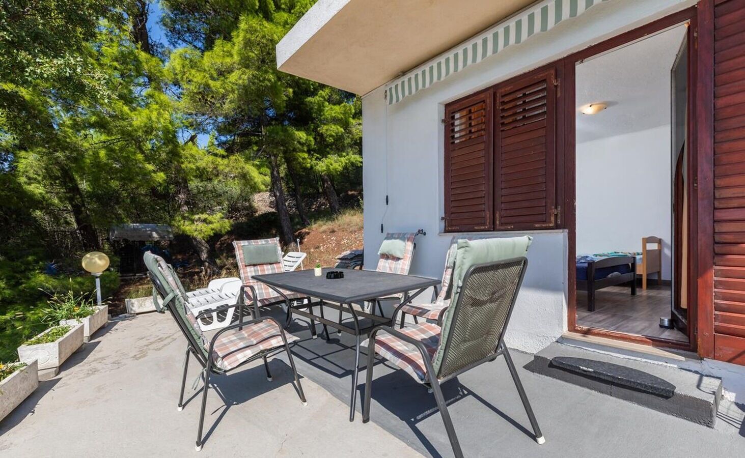 A patio with a table and chairs, a small garden, and a building with a sliding door.