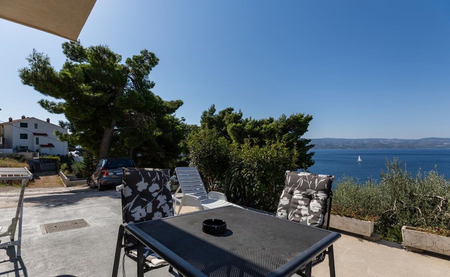 Eine Terrasse mit zwei Liegestühlen und einem Tisch, mit Blick auf ein Gewässer und eine entfernte Küstenlinie.