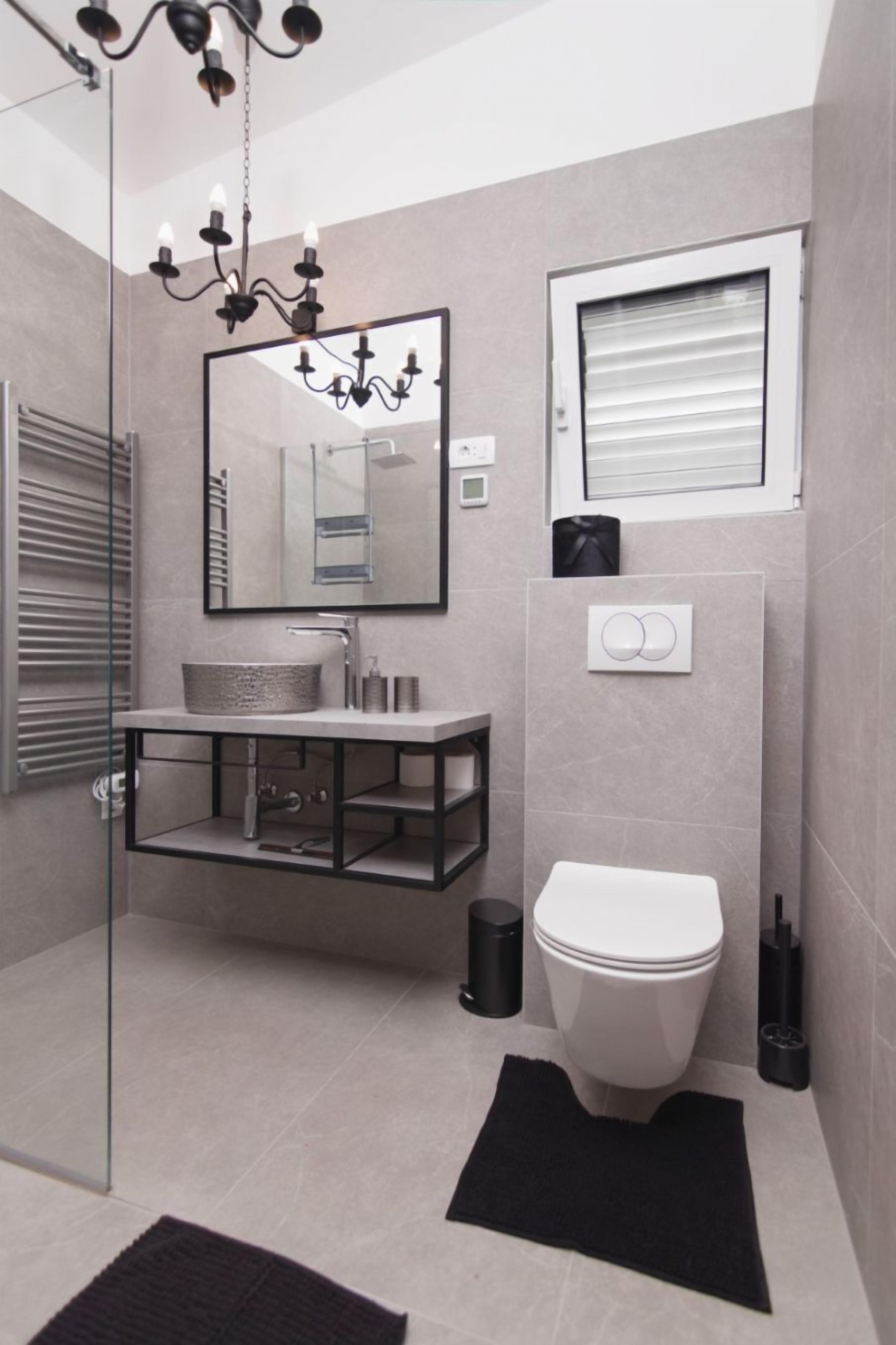 Um banheiro moderno com box de vidro, pia independente, vaso sanitário e lustre.