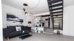 A modern living room with a black sofa, a coffee table, and a staircase leading to a kitchen area. - House Nika (Punat)