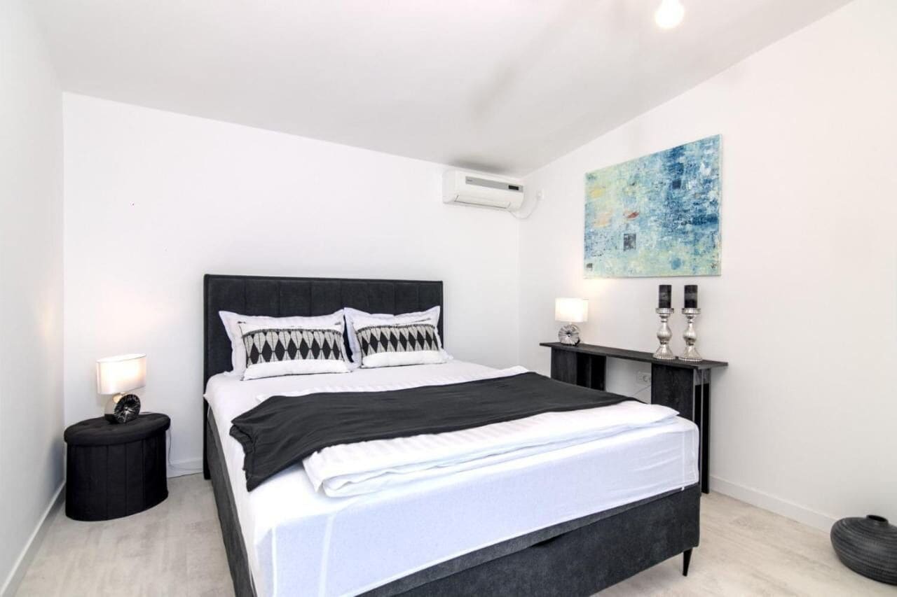 Quarto moderno com cabeceira preta, roupa de cama branca e mesa de cabeceira com abajur.