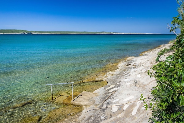 A beach with clear water, steps leading into the sea, and a distant shoreline. - Apartment Ivo (Razanac)