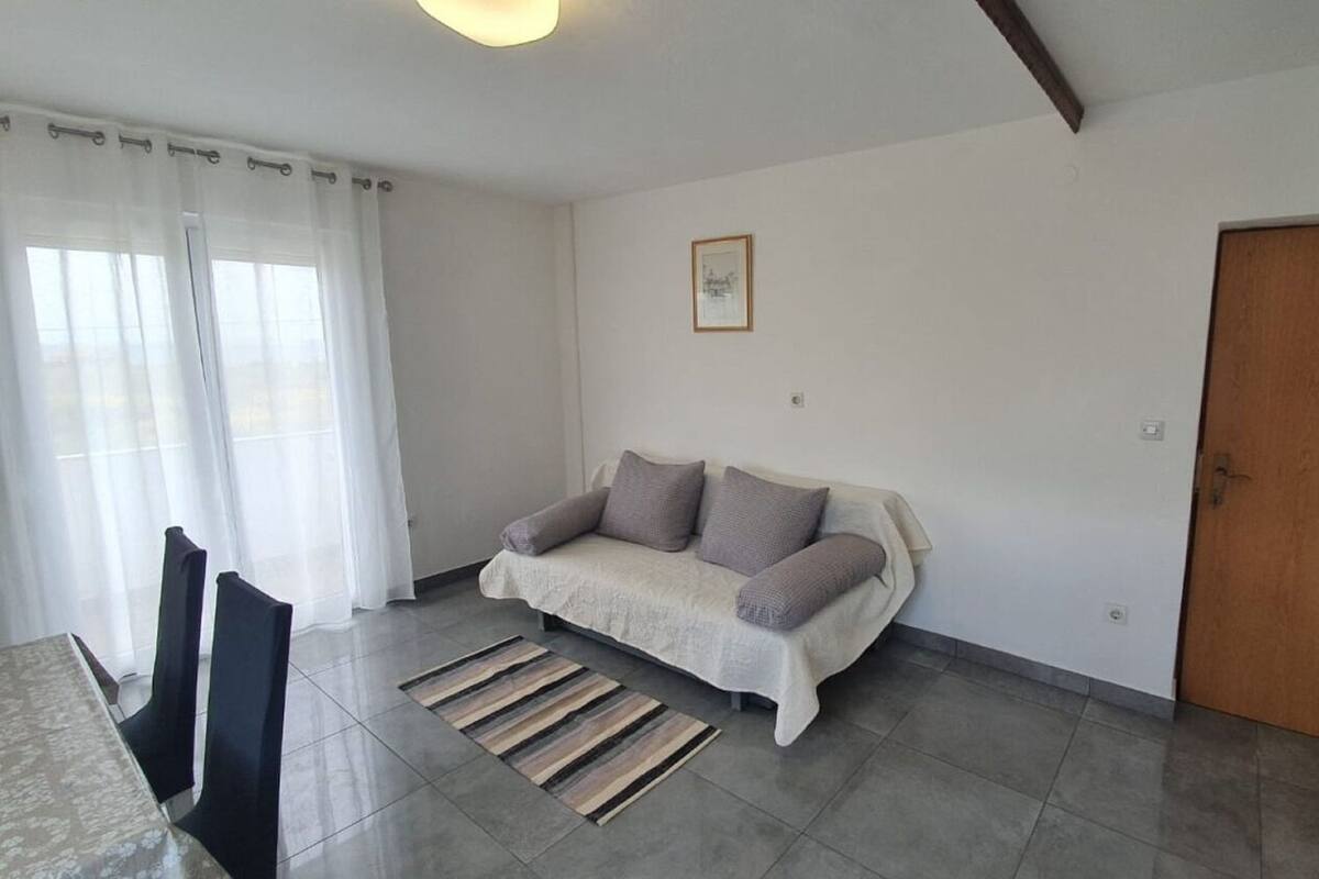 A living room with a sofa, a dining table with chairs, a wooden door, and a window with curtains.