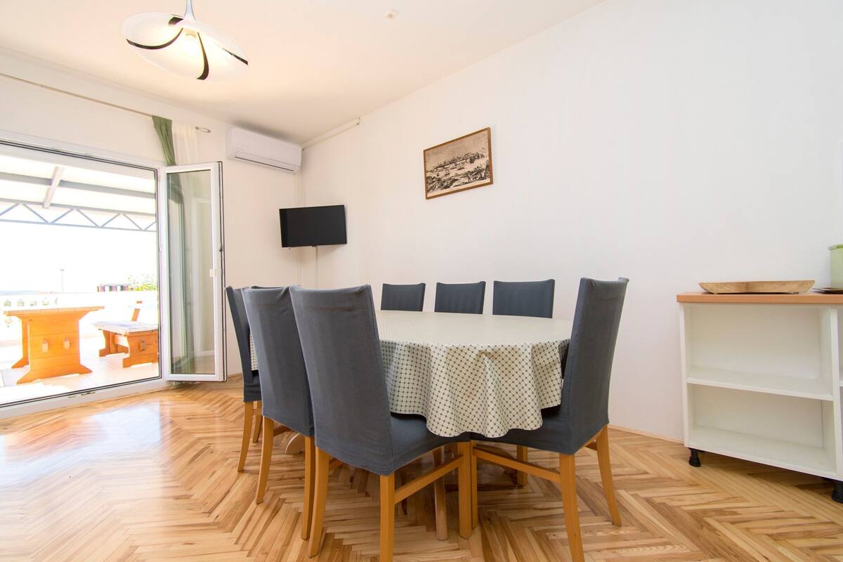 A dining area with a table and chairs, a television on the wall, and a picture frame.