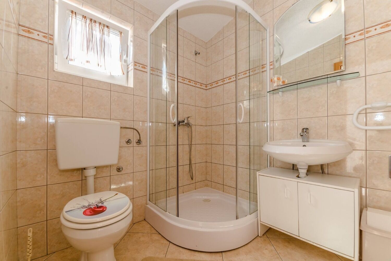 A bathroom with a glass-enclosed shower, a toilet, a sink, and a cabinet.