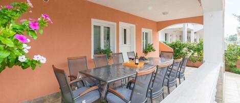 A covered outdoor dining area with a table and chairs, potted plants, and a view of the surrounding buildings.