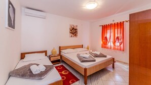 Una habitación con dos camas, un tapete rojo, una lámpara en el techo y un ventanal con cortinas rojas.
