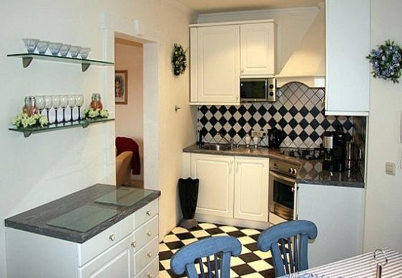 Cozinha compacta com armários brancos, piso quadriculado preto e branco e mesa com tampo de vidro.
