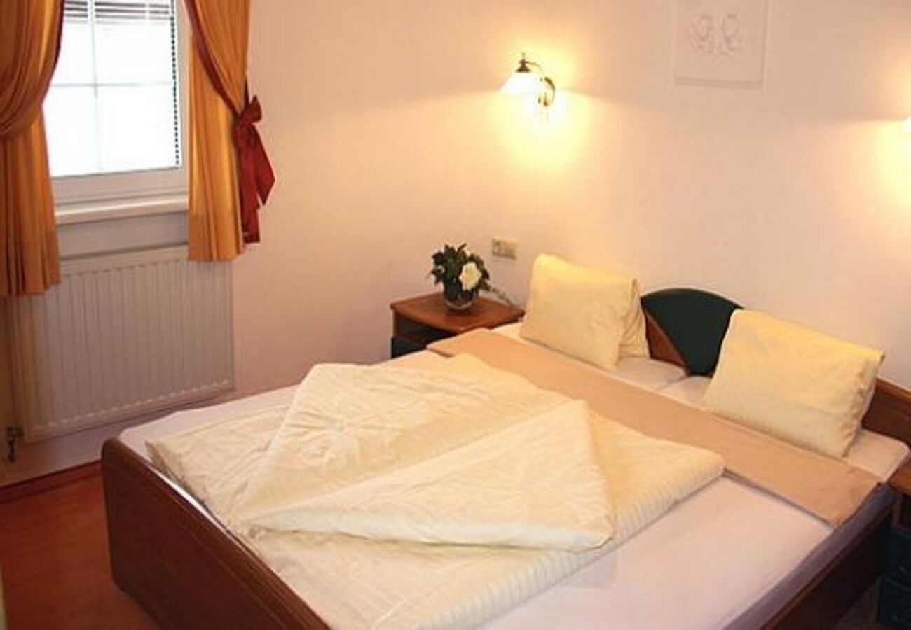 Ein Schlafzimmer mit einem Bett, einem Nachttisch mit Lampe und einem Fenster mit Vorhängen.