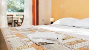 A neatly made bed with folded white towels, a floral-patterned quilt, and a view of an outdoor area with a table and chairs. - Apartments Sime (Novalja)