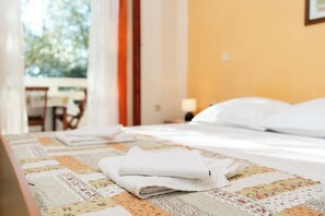 A neatly made bed with folded white towels, a floral-patterned quilt, and a view of an outdoor area with a table and chairs. - Apartments Sime (Novalja)