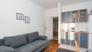 A compact living space with a grey sofa, a kitchen with blue cabinets, and a small rug. - Apartments Sime (Novalja)