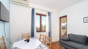 A room with a dining table, chairs, a sofa, a TV, and a window with curtains. - Apartments Sime (Novalja)