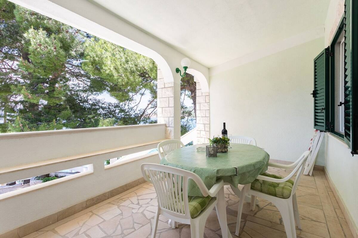 A covered outdoor seating area with a table and chairs, a bottle of wine, and a view of trees through a window.