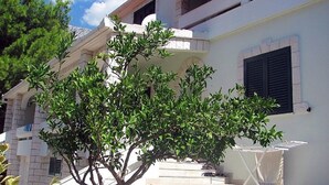 Un bâtiment blanc avec un arbre devant, un balcon et un escalier menant à l’entrée.