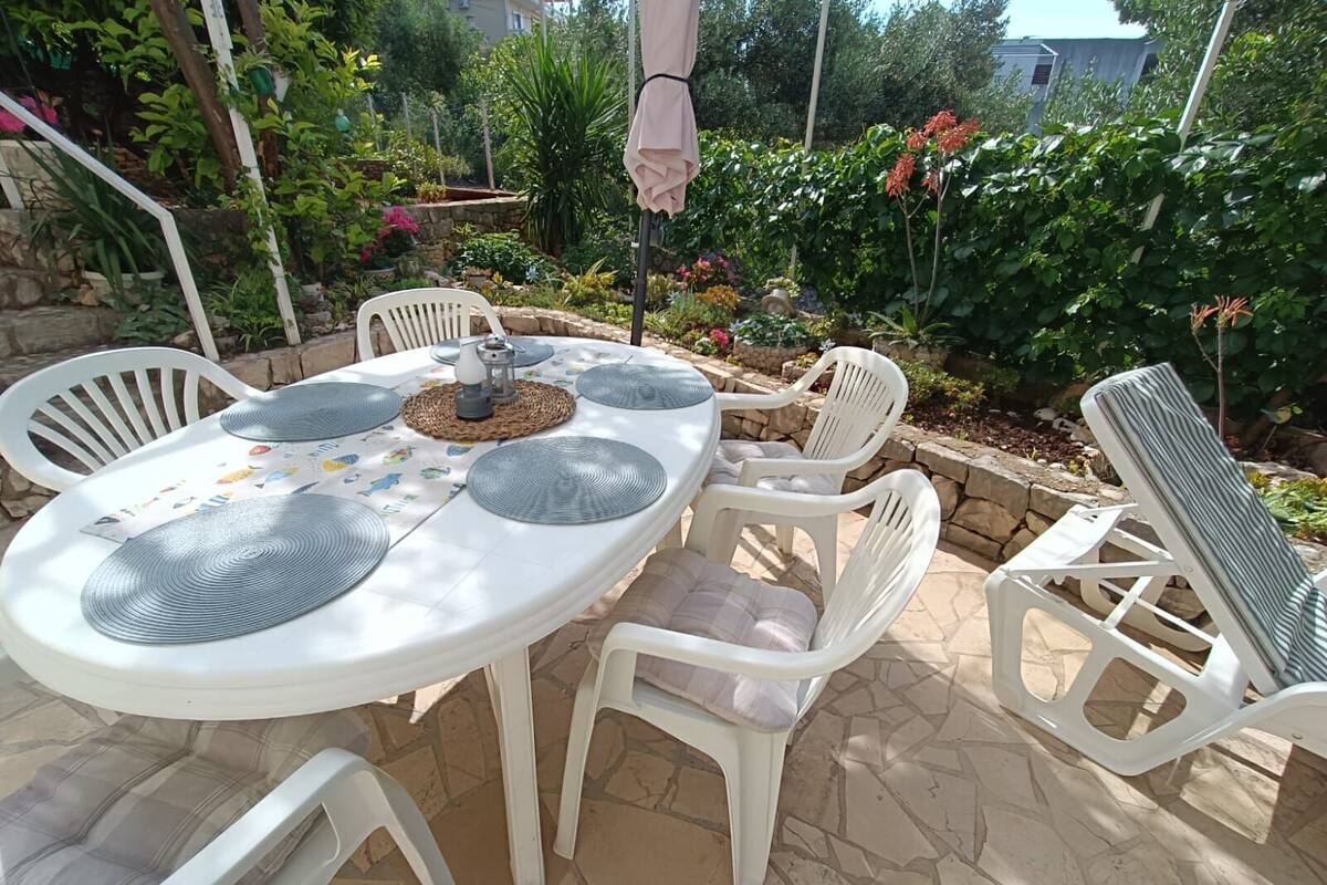 An outdoor patio with a round table, white plastic chairs, and a woven placemat.