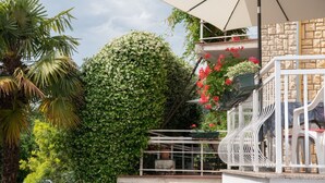 A balcony with white railings, a white umbrella, and red flowers. - Apartment Miriam (Opatija)