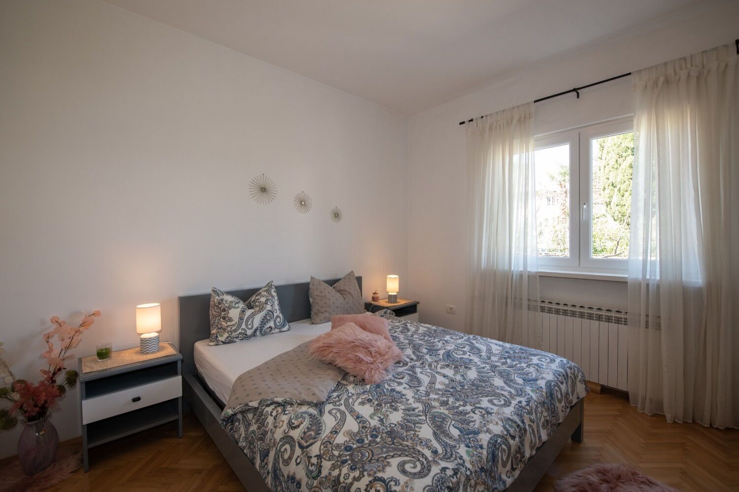 Ein Schlafzimmer mit Bett, Nachttischen, einem Fenster mit Vorhängen und Wanddekorationen.