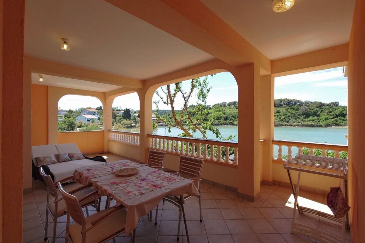 A balcony with a table and chairs, a sofa, and a view of a lake and greenery.