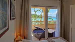 Hotelkamer met een bed, een tafeltje met een lamp en uitzicht op een balkon met een stoel en een tafel.