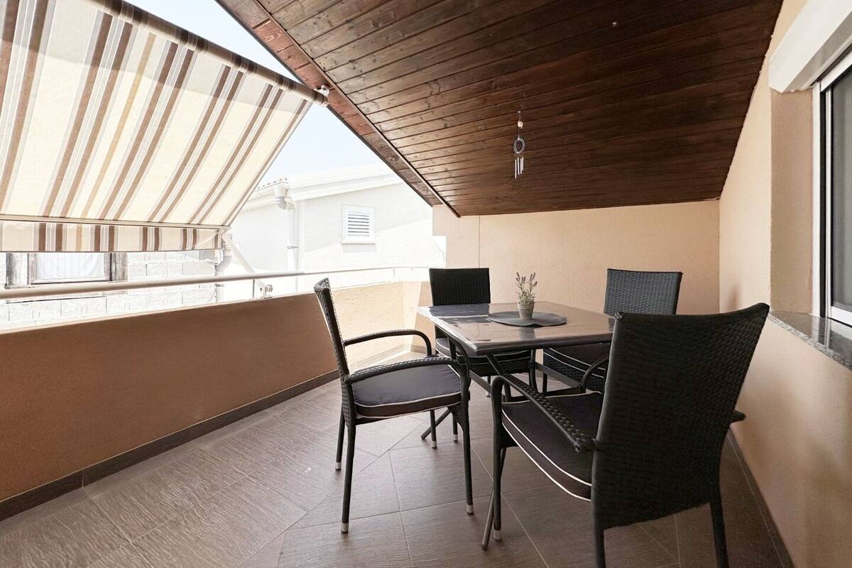 A balcony with a wooden ceiling, a table with chairs, and a view of buildings.