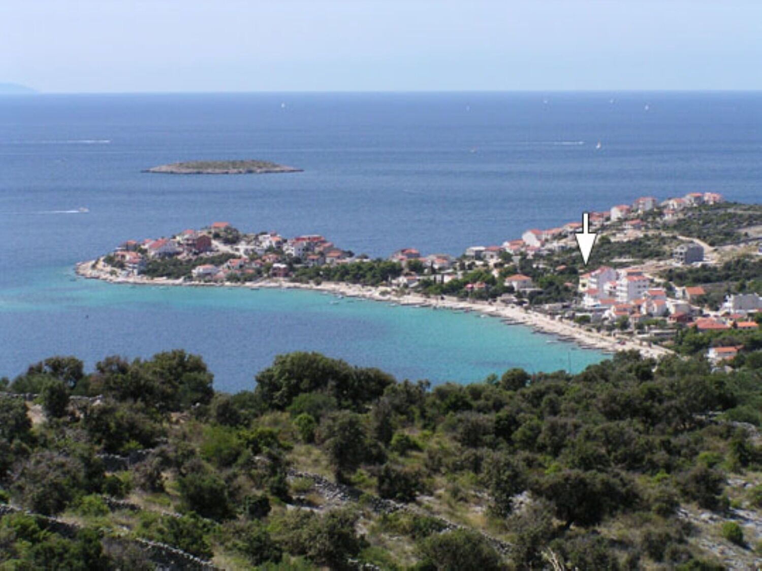 Eine Küstenstadt mit Gebäuden entlang der Uferlinie, eine kleine Insel in der Nähe und eine hügelige Landschaft im Vordergrund.