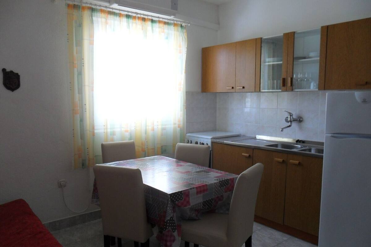 Une cuisine de taille réduite comprenant une table à manger, des chaises, un réfrigérateur et des armoires en bois.
