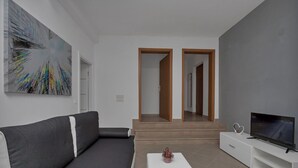 A modern living room with a gray sofa, a white coffee table, a flat-screen TV, and a large abstract painting on the wall. - Apartment Petar (Makarska)