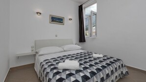 A bedroom with a bed, a nightstand, a window with curtains, and a wall-mounted air conditioner. - Apartment Petar (Makarska)