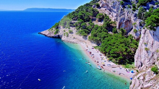 A coastal beach with clear blue waters, rocky cliffs, and lush greenery. - Apartment Petar (Makarska)