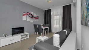 A modern living room with a grey sofa, a white TV stand, a dining table with chairs, and a large abstract painting on the wall. - Apartment Petar (Makarska)
