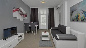 A modern living room with a flat-screen TV, a sofa, a dining table with chairs, and artwork on the walls. - Apartment Petar (Makarska)