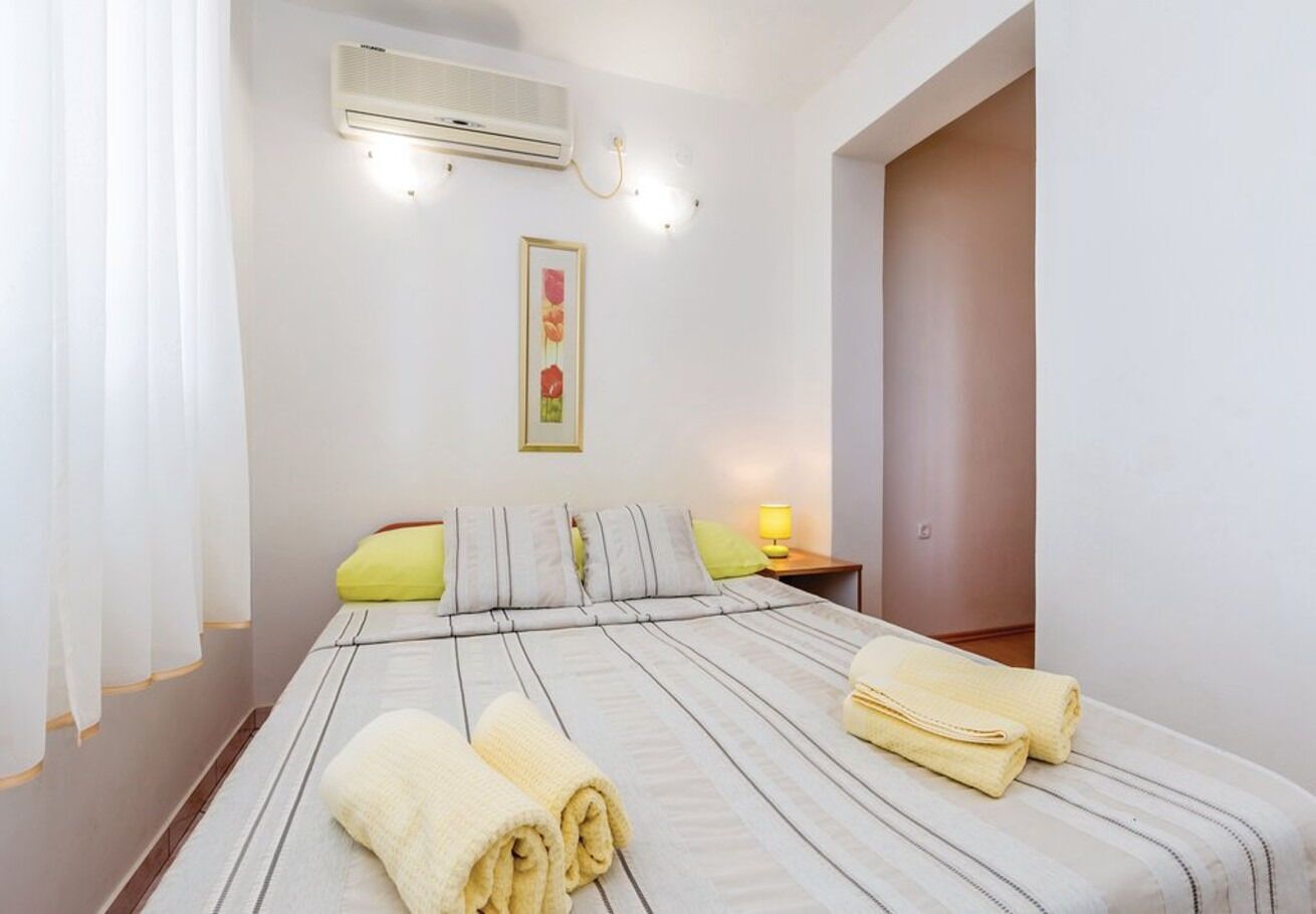 A hotel room with a bed, a nightstand, an air conditioner, a wall-mounted light, and a framed picture.