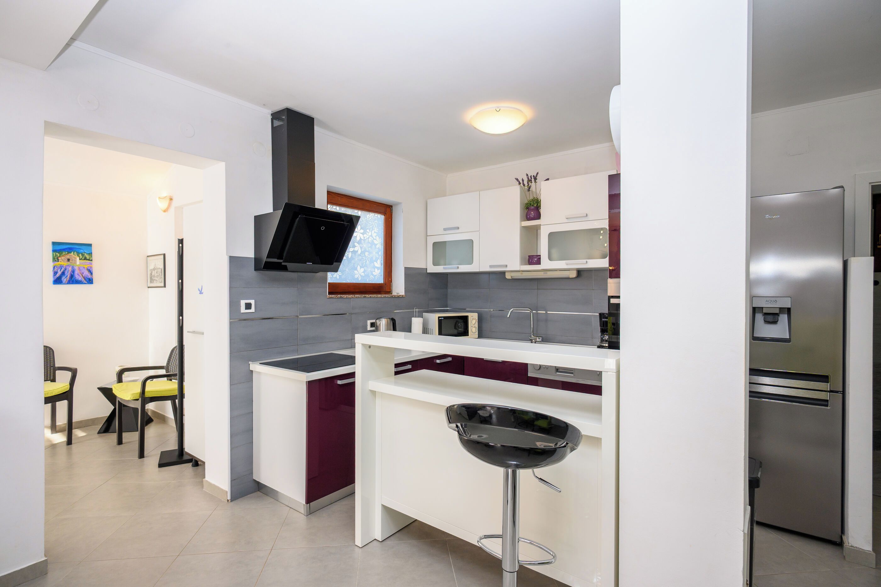 A modern kitchen with a built-in microwave, a stainless steel refrigerator, and a bar stool.