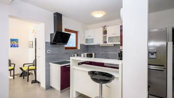 A modern kitchen with a built-in microwave, a stainless steel refrigerator, and a bar stool.
