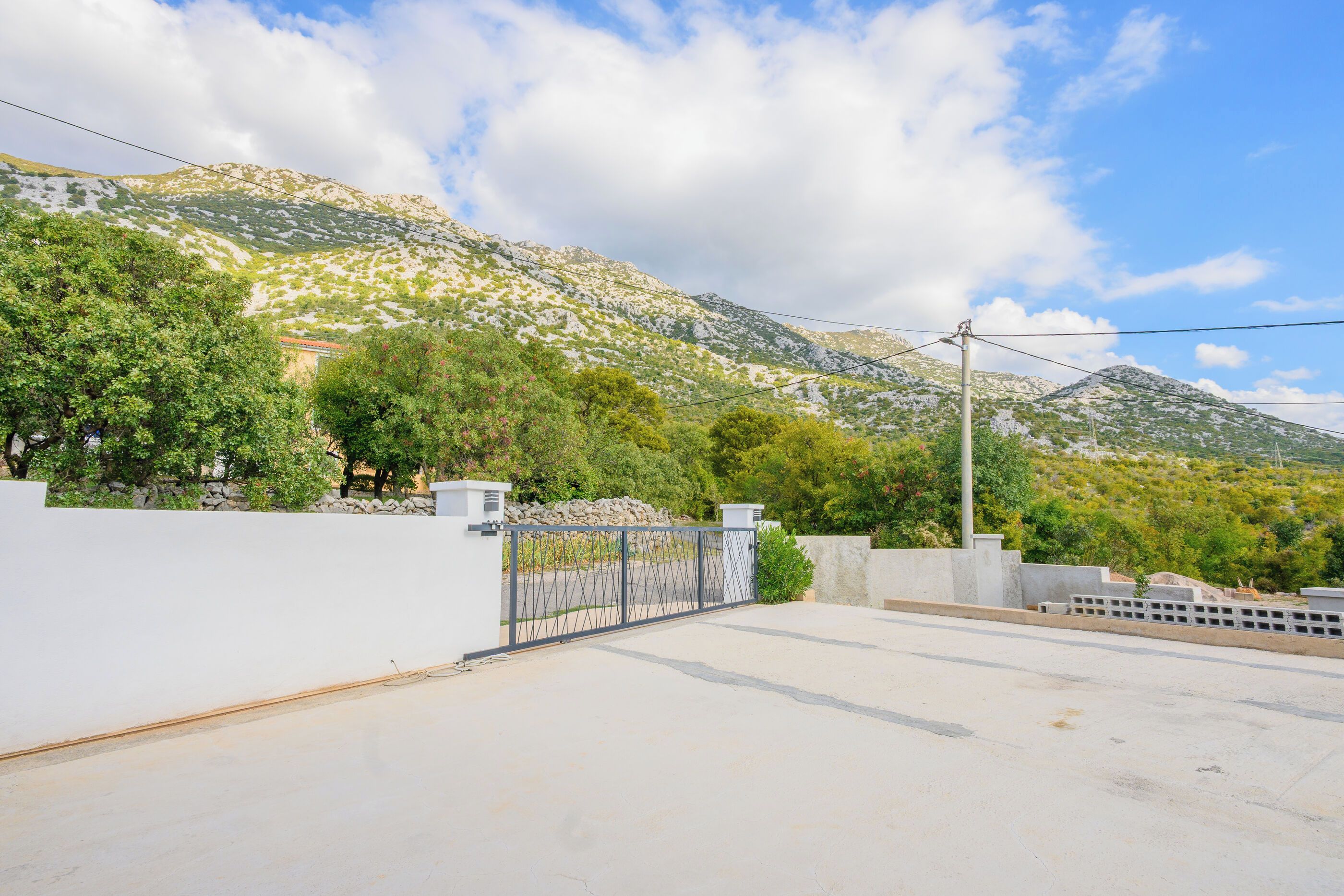 Um bairro residencial com portão de acesso, muro branco e montanhas ao fundo.