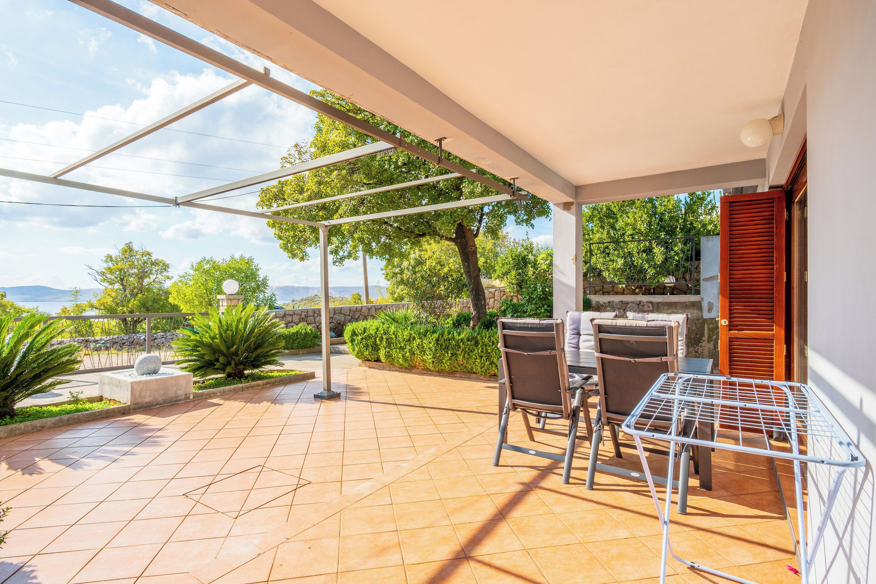 Un patio cubierto con suelo de baldosas, mobiliario exterior y vistas al paisaje.