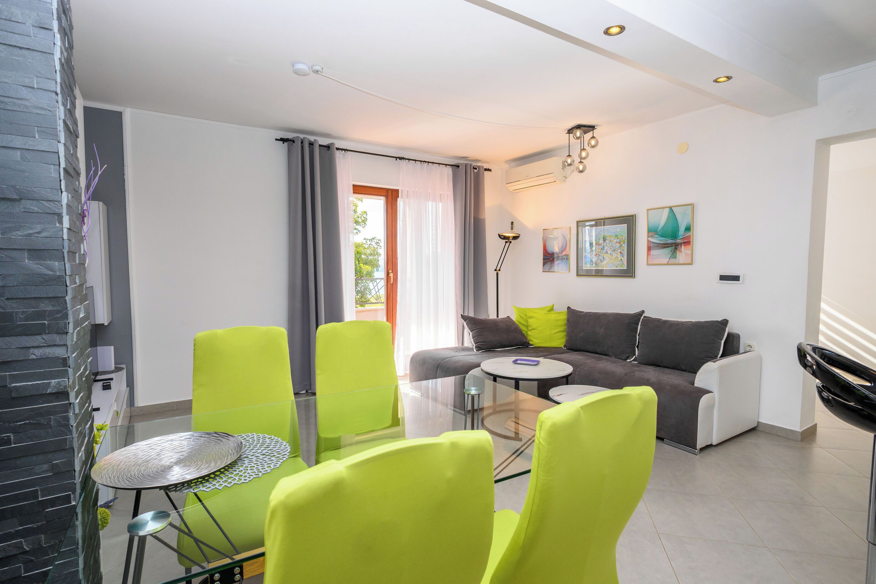 Una sala de estar moderna con un sofá, sillas verde brillante, una mesa de centro de vidrio y una mesa de comedor.