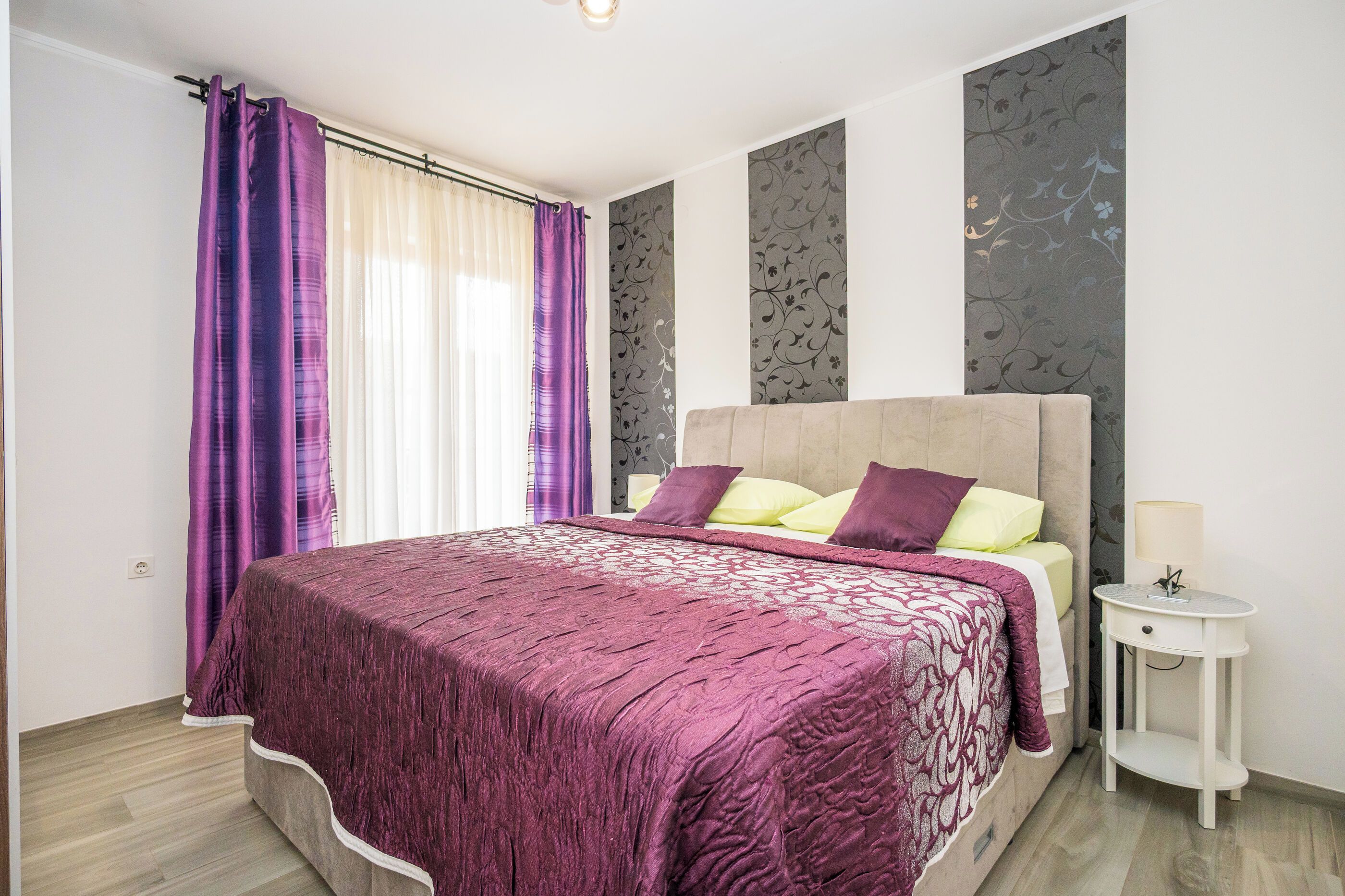 A bedroom with a large bed, a nightstand, and a window with curtains.