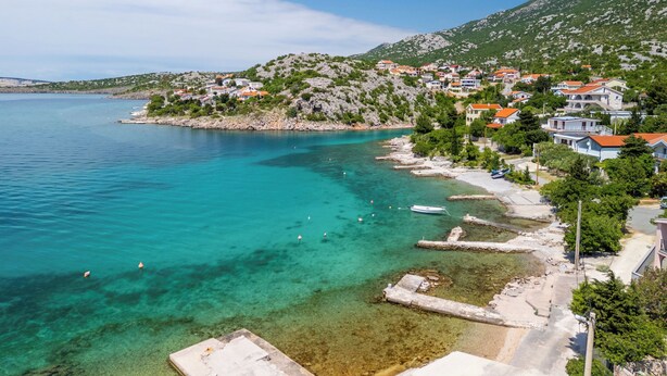 A coastal village with houses along the shoreline, clear turquoise waters, and rocky hills in the background. - Apartments Ivni (Karlobag)