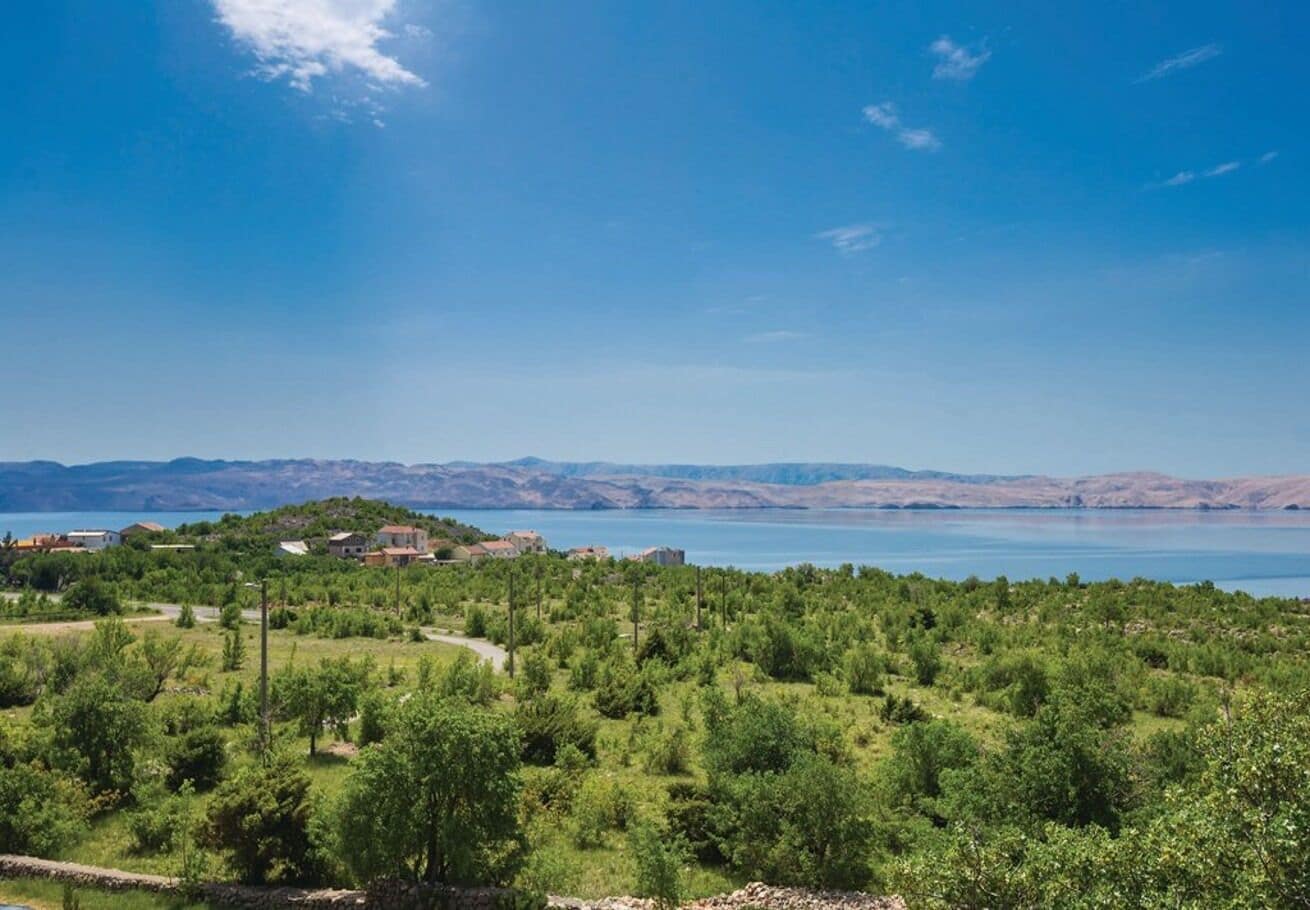 Un paisaje costero con una vista despejada del mar, un sendero que atraviesa una zona verde y edificios al fondo.