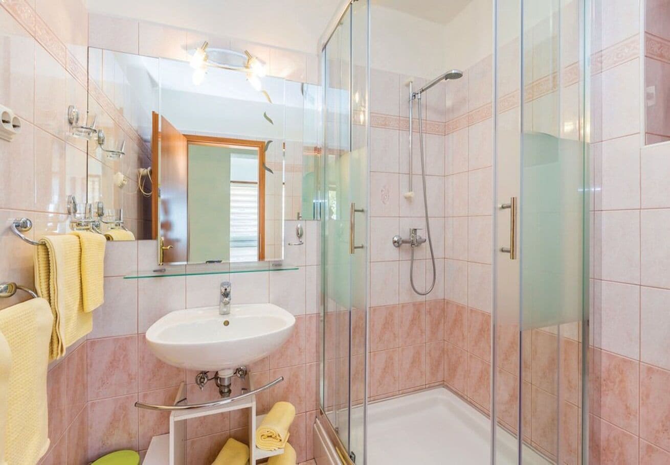 A modern bathroom with a glass shower enclosure, a sink with a mirror, and a towel rack.