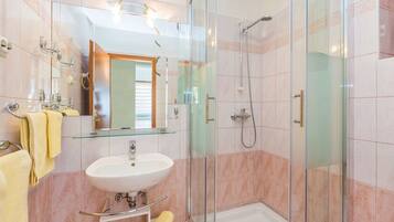 A modern bathroom with a glass shower enclosure, a sink with a mirror, and a towel rack.