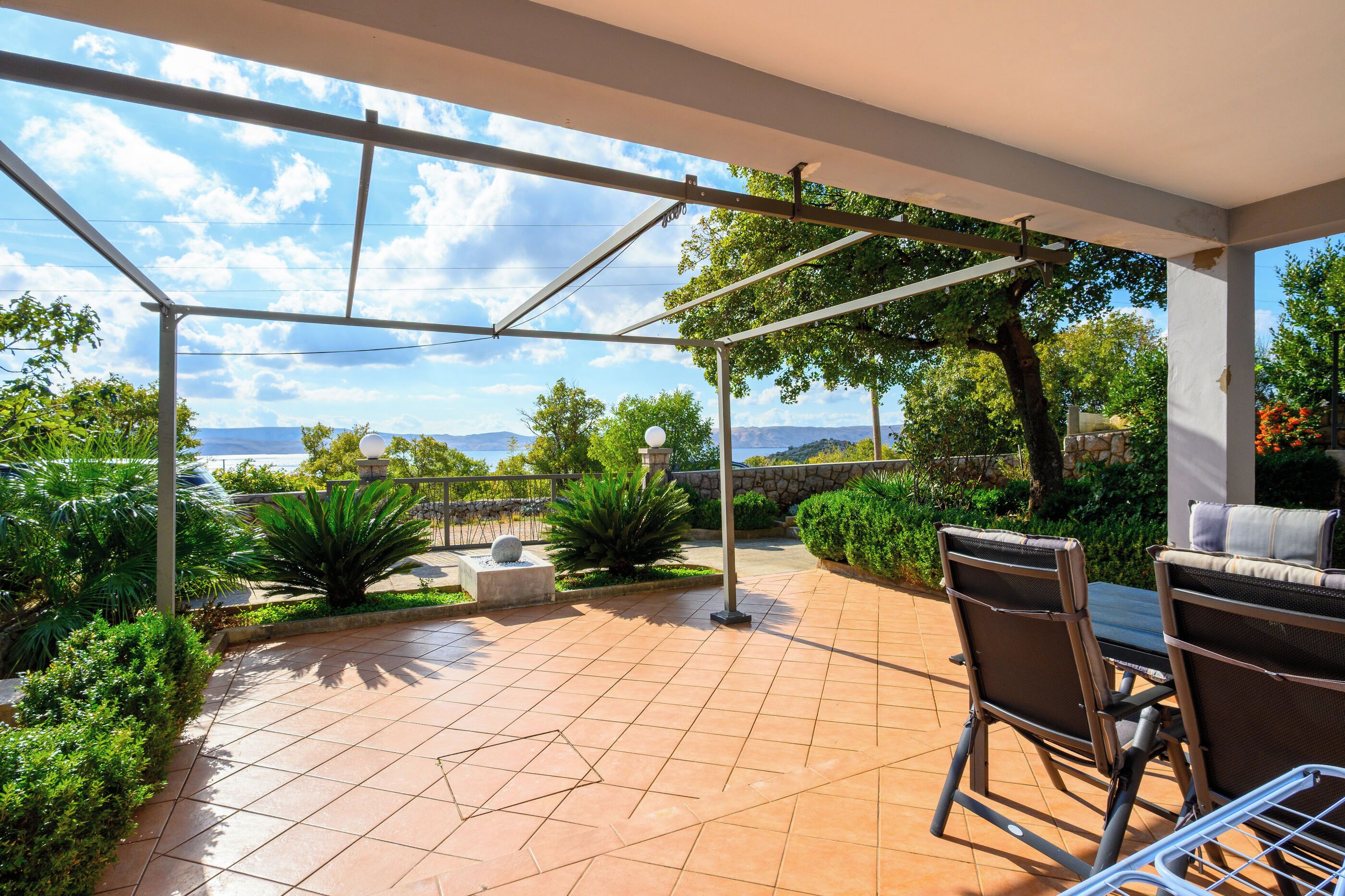 A covered patio with a view of the sea, outdoor furniture, and a stone wall.